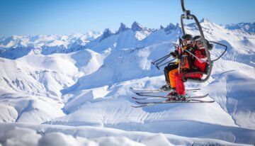 Skifahrer im Sessellift vor schneebedeckter Berglandschaft | © Cyrille Quintard / Alpe d’Huez Tourisme