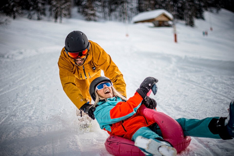 Mann schiebt Frau auf einem rosa Reifen im Schnee. | © Weare Merci