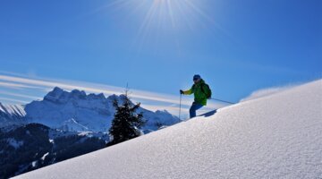 Skier on a snow-covered slope with mountains in the background | © JFVuarand