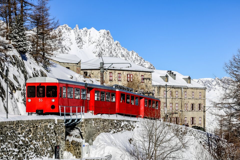 Red train in front of snowy mountain scenery and hotel | © Office de Tourisme Vallée de Chamonix / Morgane Raylat