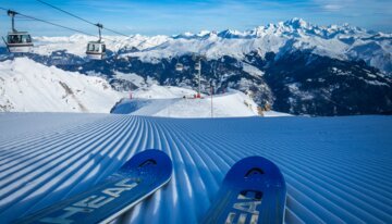 Skis on groomed slope with mountain view | © Courchevel Tourisme