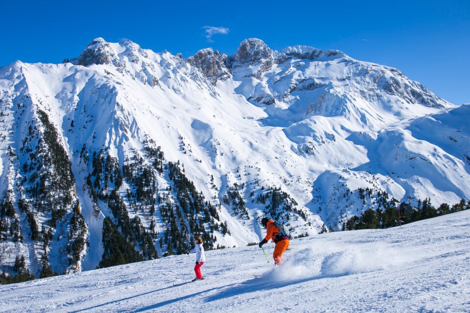 Two skiers on a snow-covered slope with mountains in the background. | © Courchevel Tourisme
