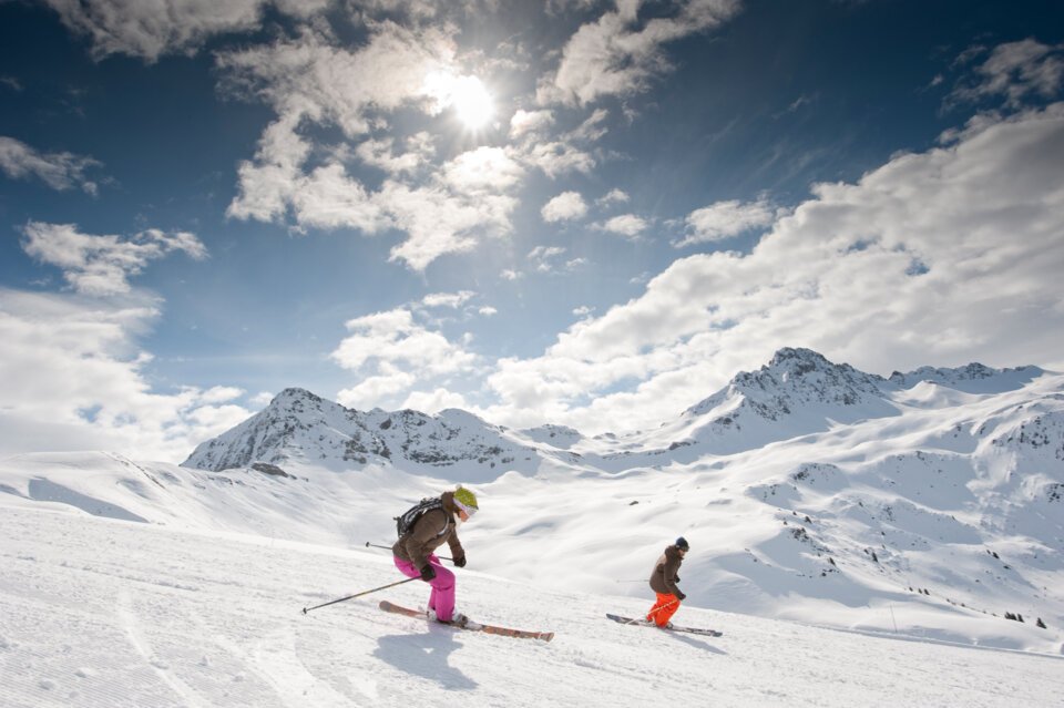 Two skiers on a snowy slope with mountains in the background. | © Gilles Lansard