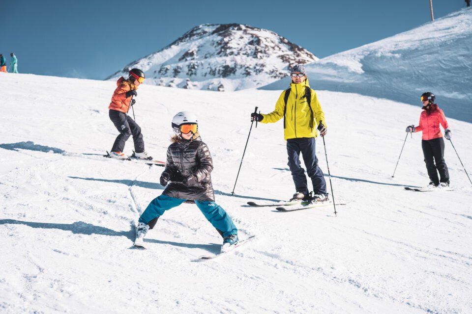 Skiers on a ski slope with snow-covered mountains in the background. | © Les 2 Alpes / Luka Leroy