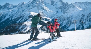 Skifahren mit Kindern vor verschneitem Bergpanorama. | © Yucca Films