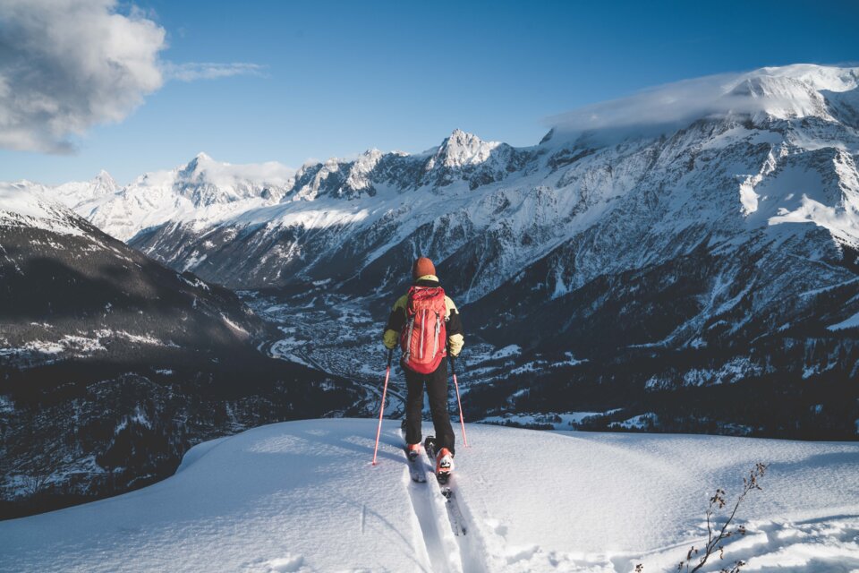 Skifahrer mit rotem Rucksack blickt auf verschneite Berge | © Yucca Films