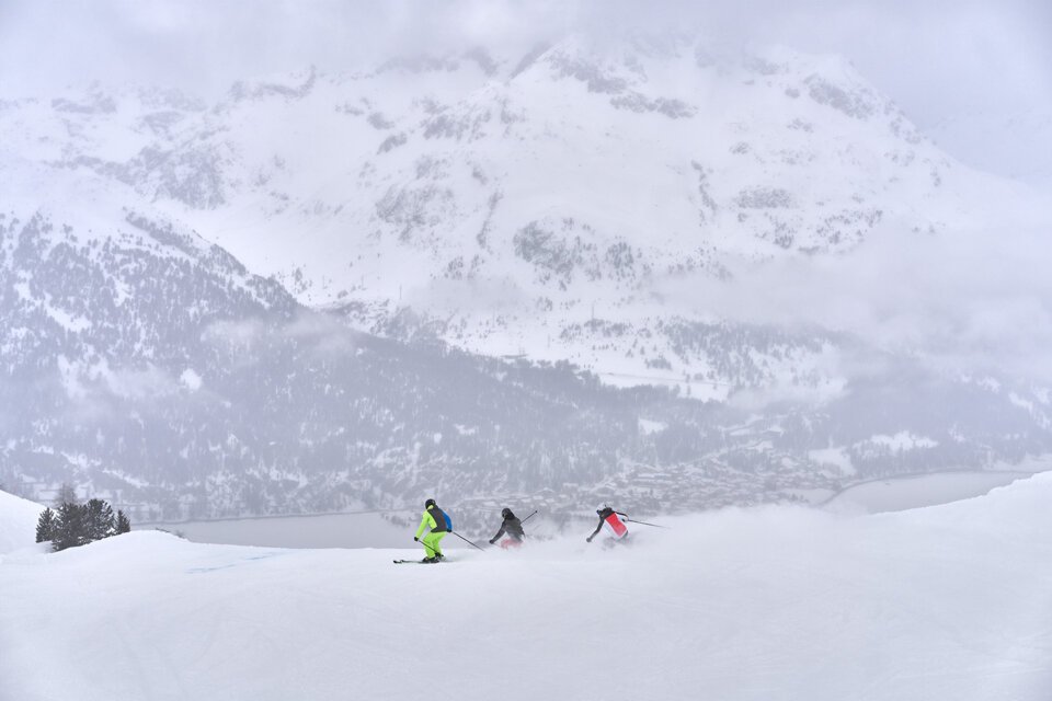Trois skieurs sur une piste enneigée avec une montagne en arrière-plan.
