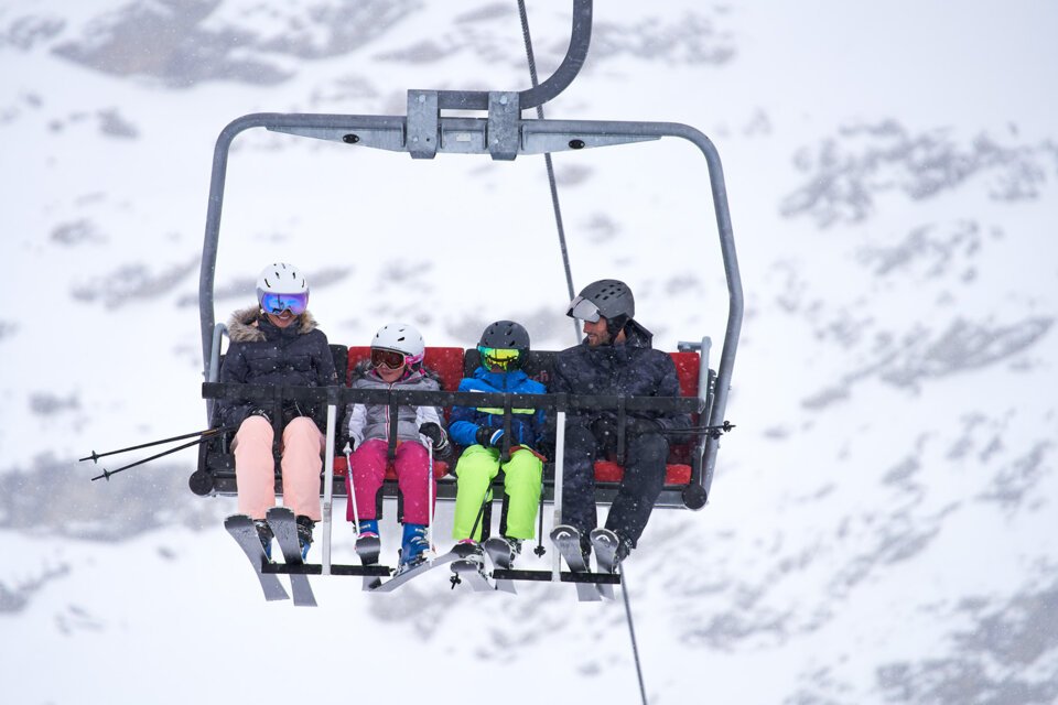 Famille prenant un télésiège sous la neige.