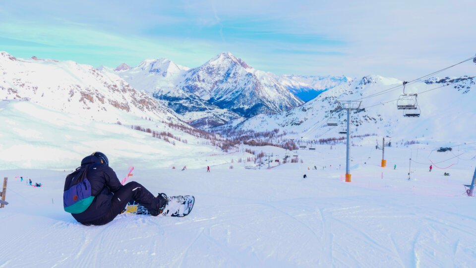 Snowboarder sitting in a snowy mountain landscape. | © Florian COLAS / Office de Tourisme de Montgenèvre