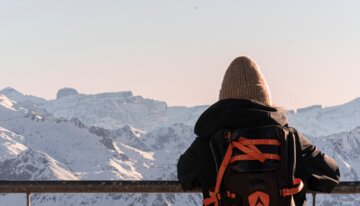 Person mit Rucksack blickt auf schneebedeckte Berge | © Remi Férodet