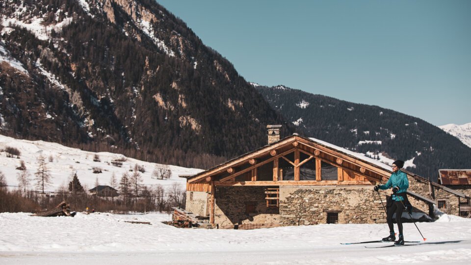 Skier in front of a mountain house in a snowy landscape | © Sophie Planque / Ski de fond