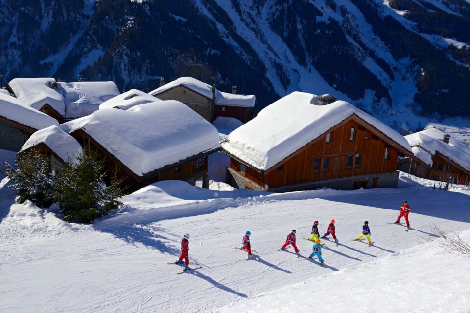 Groupe de ski et moniteur devant des maisons enneigées. | © Philippe Royer / Sainte Foy Tourisme