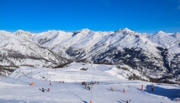 Skiers on a snowy slope with mountains in the background. | © Serre Chevalier Vallée Briançon - @laurapeythieu