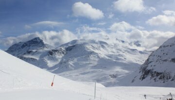 Snowy mountain landscape under a blue sky with clouds.