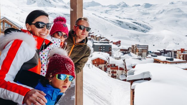 Family enjoying the view of a snowy mountain landscape from a balcony. | © OT Val Thorens