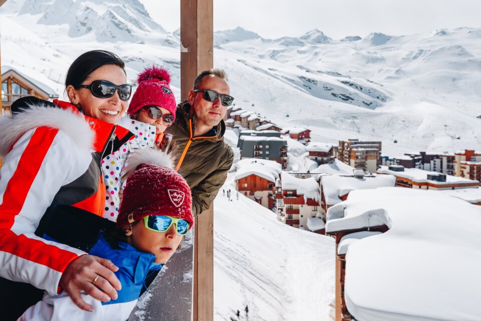 Family enjoying the view of a snowy mountain landscape from a balcony. | © OT Val Thorens