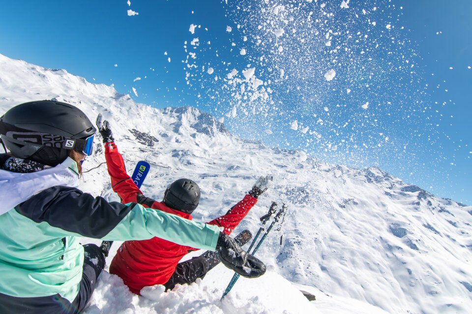 Two skiers throwing snow in the air against a snowy mountain backdrop. | © T. Loubere / OT Val Thorens