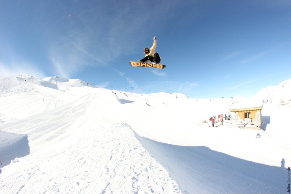 Snowboarder jumping over a snow ramp against a blue sky. | © Val d'Isère Tourisme | Julien Lecointe