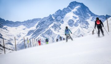 Skifahrer auf einer Skipiste mit verschneiten Bergen im Hintergrund. | © Cyrille Quintard