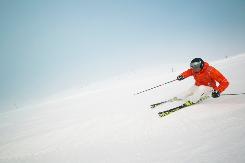 Skifahrer in oranger Jacke auf schneebedeckter Piste | © Elina Sirparanta | Visit Finnland