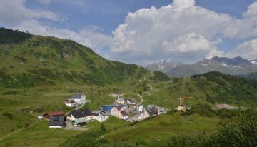 Vue panoramique d'un village alpin avec des montagnes et des nuages | © www.wikipedia.com | Friedrich Böhringer