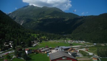 Panoramic view of an alpine village with mountains and a paraglider | © https://www.flickr.com/photos/thisisbossi/