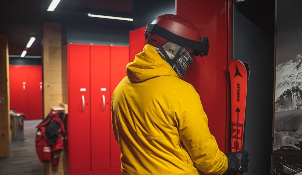 Skifahrer in gelber Jacke vor roten Schränken