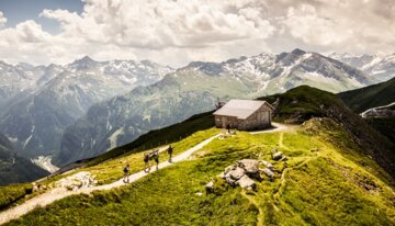 Hikers on a trail in the mountains with a cabin in the background.