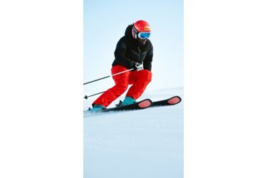 Skifahrerin in roter Hose und schwarzer Jacke fährt Ski