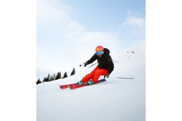 Skifahrer in roter Hose und schwarzer Jacke auf einer Skipiste.