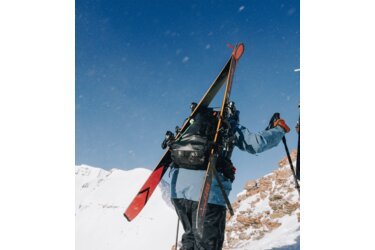 Skieur portant des skis et un sac à dos dans un paysage montagneux enneigé.