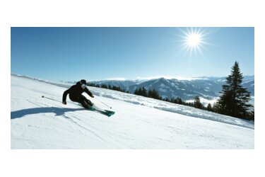 Skifahrer auf schneebedeckter Piste unter blauem Himmel.