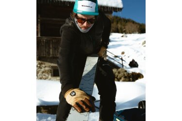 Homme tenant des skis portant un bonnet KÄSTLE dans la neige.