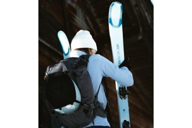 Personne portant des skis et un sac à dos, vue de dos.