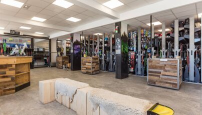 Interior view of a ski rental shop with skis, boots, and wooden seating.