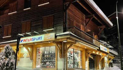 Intersport-Geschäft in verschneiter Alpenlandschaft bei Nacht