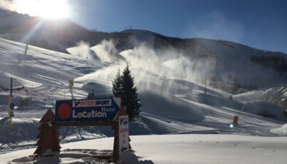Piste de ski enneigée avec canons à neige et panneau d'indication.