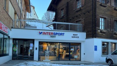 Façade d’un magasin INTERSPORT Rent dans un centre de village enneigé.